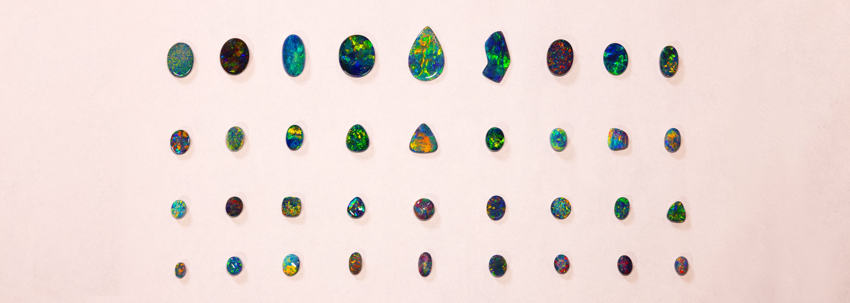 Collection of colorful black opal arranged in a grid on a light pink background from black opal direct